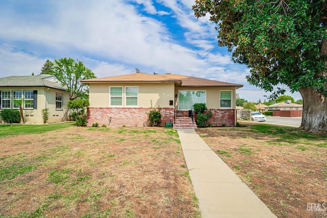 view of front of home with brick siding, a front yard, and stucco siding