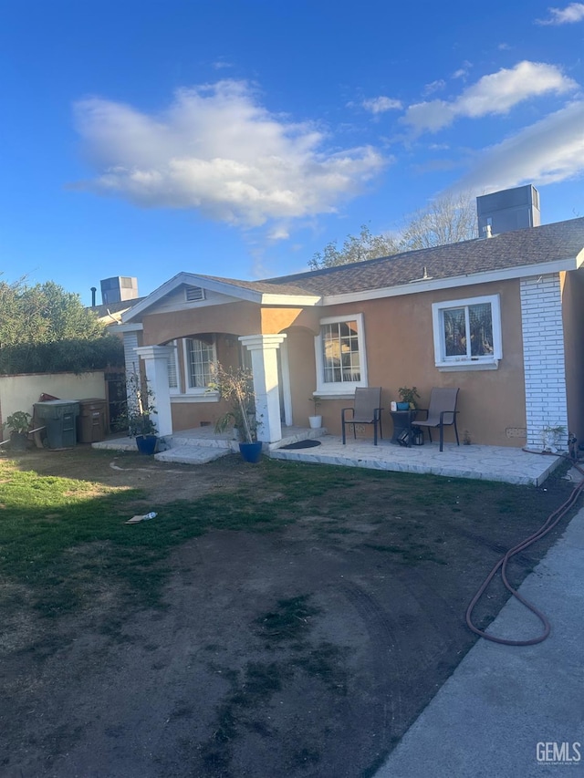 exterior space featuring a patio area, roof with shingles, and stucco siding