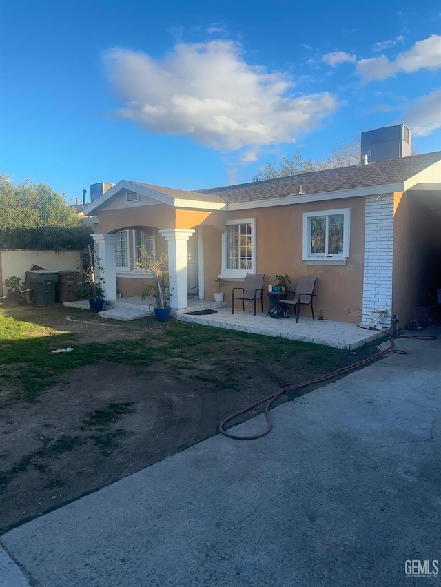 back of property featuring brick siding, roof with shingles, a patio, and stucco siding