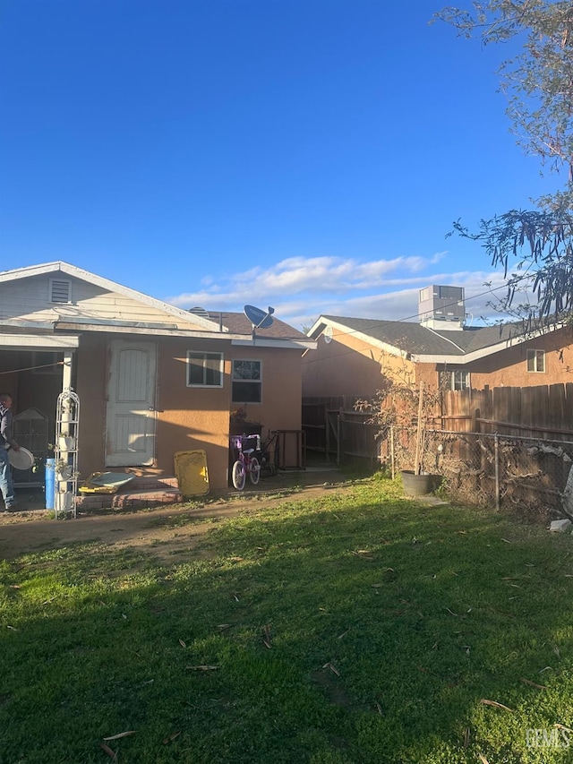 back of house featuring stucco siding, fence, and a yard