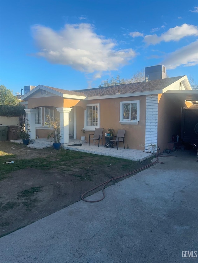 view of front of home featuring a carport, a patio area, brick siding, and stucco siding