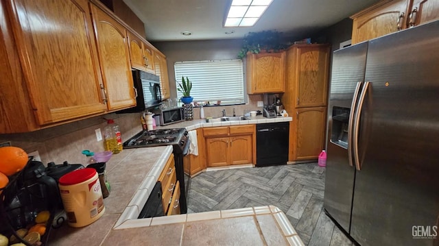 kitchen with sink, kitchen peninsula, tile countertops, light parquet flooring, and black appliances