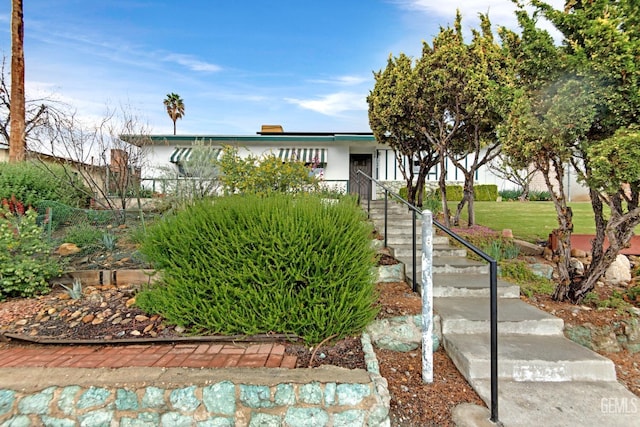 view of front facade with stucco siding, a front yard, and stairs