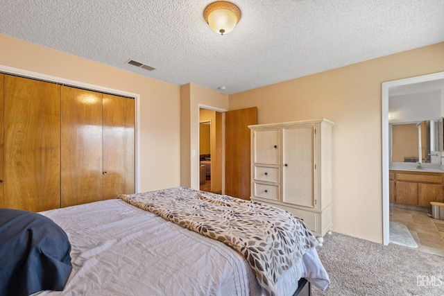 bedroom featuring a closet, light colored carpet, a textured ceiling, visible vents, and ensuite bathroom