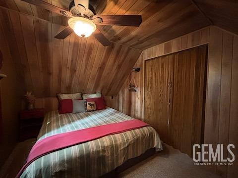 bedroom featuring wooden ceiling, vaulted ceiling, carpet flooring, a ceiling fan, and wooden walls