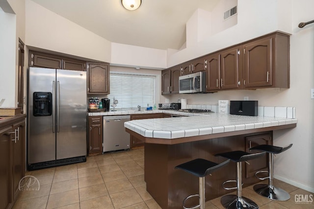 kitchen featuring appliances with stainless steel finishes, tile counters, kitchen peninsula, and light tile patterned floors