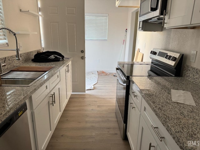 kitchen with light stone countertops, appliances with stainless steel finishes, sink, light hardwood / wood-style flooring, and white cabinets