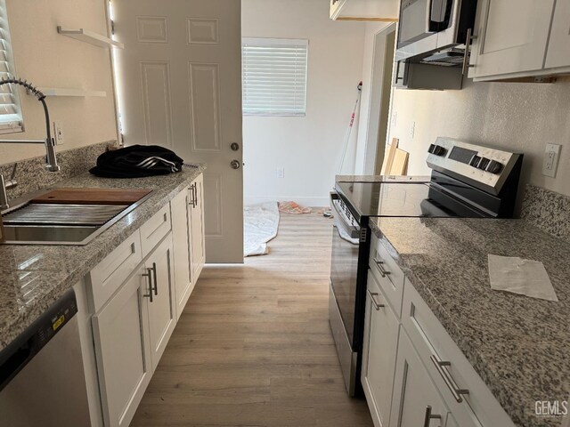 kitchen with light stone countertops, appliances with stainless steel finishes, sink, light hardwood / wood-style flooring, and white cabinets