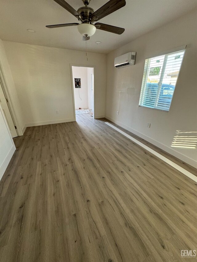 empty room with ceiling fan, wood-type flooring, and a wall mounted air conditioner