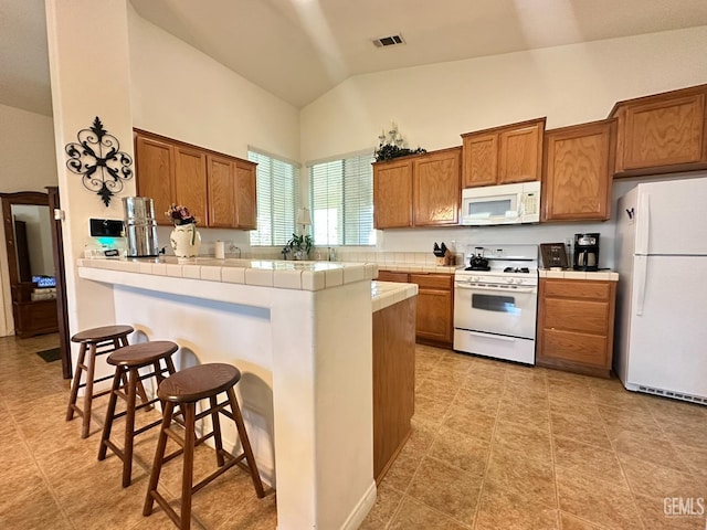 10304 Blythe Ct, Bakersfield, CA 93311 - kitchen featuring white appliances, tile counters, brown cabinetry, a breakfast bar, and a peninsula