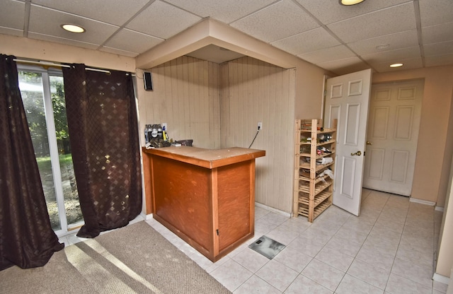 bar with light tile patterned flooring, a drop ceiling, a bar, and baseboards