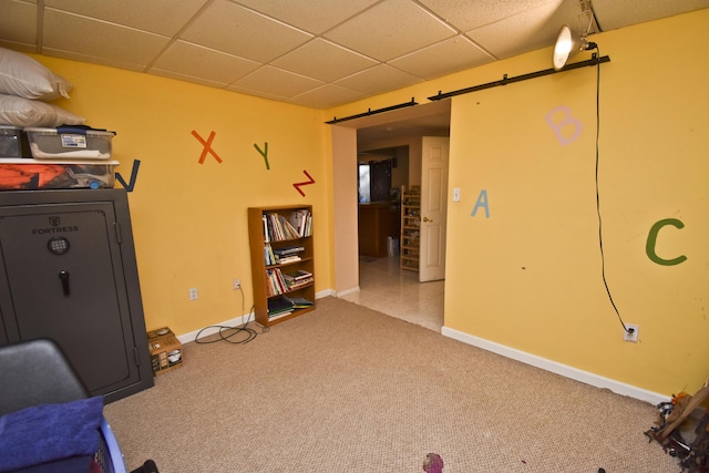 interior space featuring a barn door, a drop ceiling, baseboards, and carpet floors