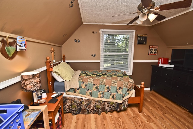 bedroom with ceiling fan, a textured ceiling, lofted ceiling, and wood finished floors