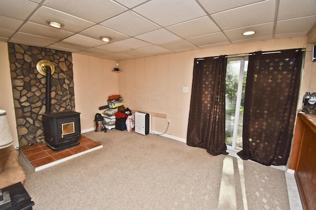 interior space with a drop ceiling, a wood stove, and carpet