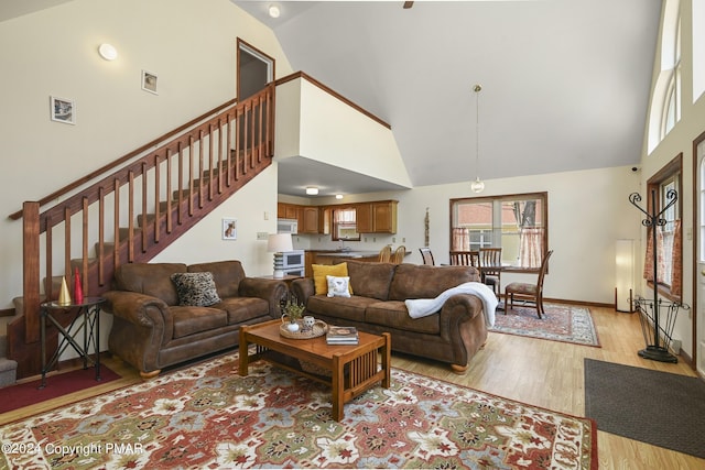 living area featuring stairs, high vaulted ceiling, light wood-style flooring, and baseboards