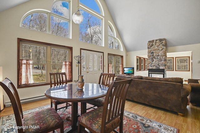 dining room with a baseboard heating unit, high vaulted ceiling, a stone fireplace, and wood finished floors