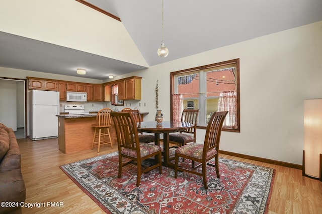 dining room with light wood-style floors, high vaulted ceiling, and baseboards