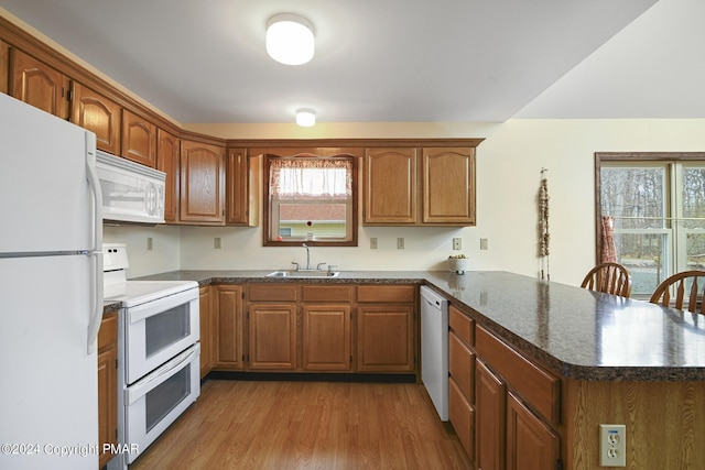 kitchen with a peninsula, white appliances, wood finished floors, a sink, and brown cabinetry