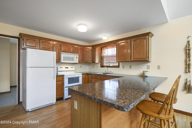 kitchen featuring light wood-style flooring, a peninsula, white appliances, a breakfast bar, and dark countertops