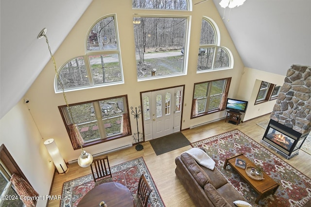 living room featuring high vaulted ceiling, wood finished floors, a wealth of natural light, and a stone fireplace