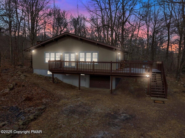 back of house at dusk with dirt driveway, stairway, a wooden deck, and a garage