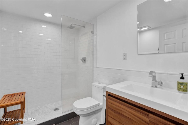 full bath featuring a walk in shower, toilet, a wainscoted wall, vanity, and tile walls