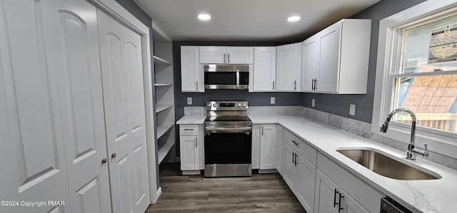 kitchen with open shelves, appliances with stainless steel finishes, white cabinets, a sink, and light stone countertops