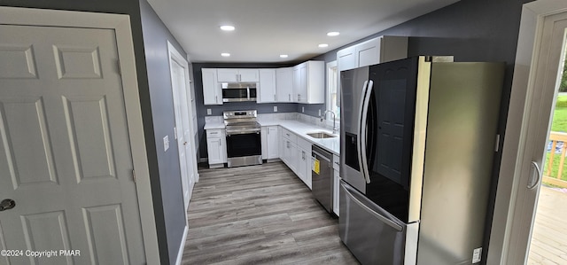 kitchen with a sink, appliances with stainless steel finishes, light wood-style flooring, and white cabinets