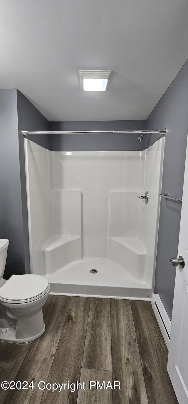 bathroom featuring a baseboard radiator, toilet, a shower, and wood finished floors