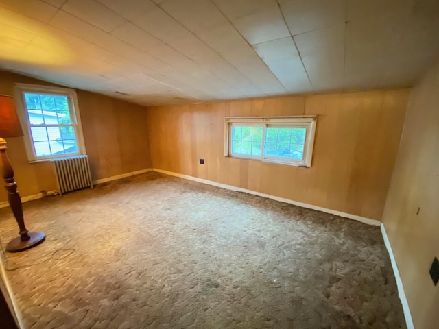 additional living space featuring radiator heating unit, plenty of natural light, carpet, lofted ceiling, and wood walls