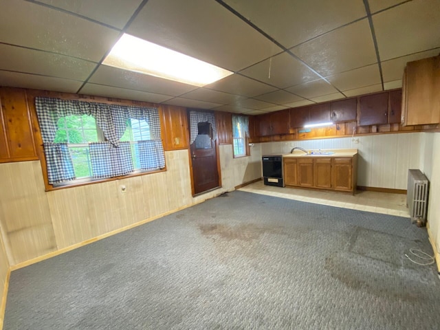 basement with radiator, a paneled ceiling, baseboards, wood walls, and carpet flooring