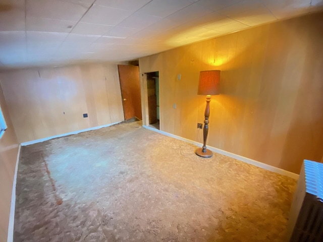 spare room featuring carpet flooring, wooden walls, and baseboards