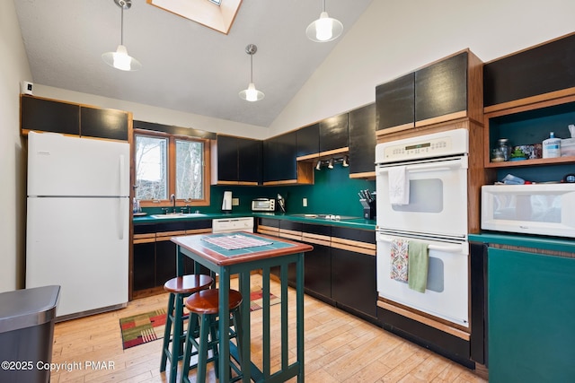 kitchen with dark countertops, hanging light fixtures, dark cabinets, a sink, and white appliances