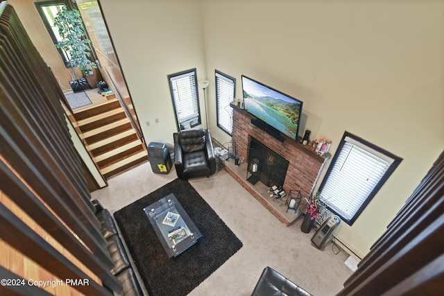 living area with a wealth of natural light, carpet floors, a high ceiling, and a brick fireplace