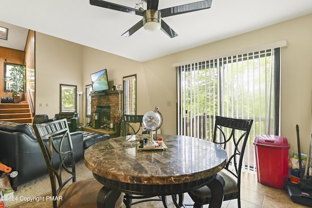 dining area featuring light tile patterned floors, a brick fireplace, ceiling fan, and vaulted ceiling