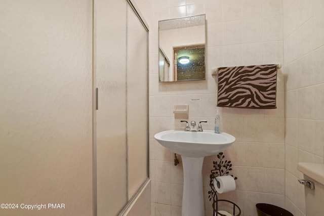 full bathroom with tile walls, toilet, a shower with door, and a sink