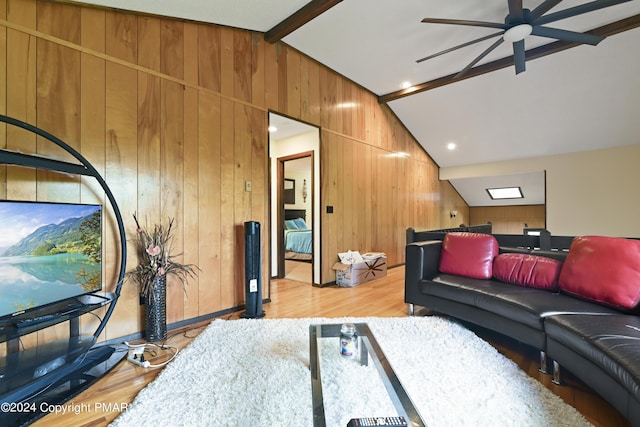 living area featuring wooden walls, vaulted ceiling with beams, light wood-type flooring, and a ceiling fan