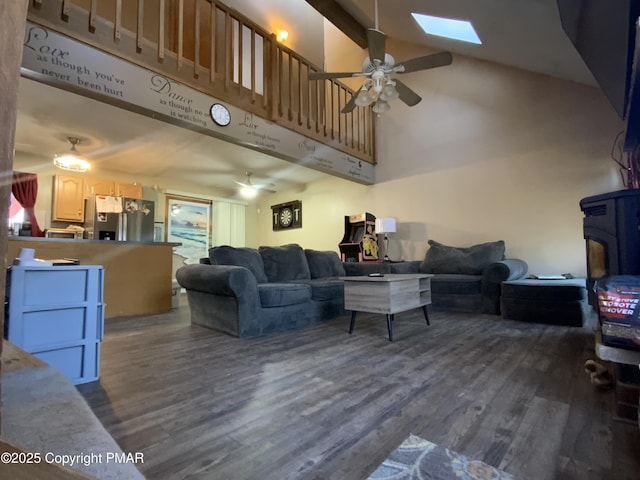 living area with ceiling fan, a skylight, a wood stove, high vaulted ceiling, and dark wood-style flooring