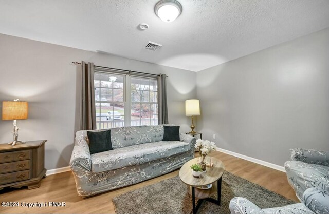 living room with visible vents, a textured ceiling, baseboards, and wood finished floors