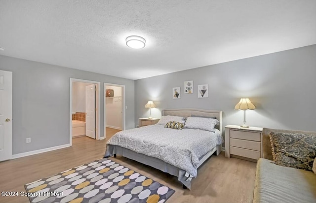 bedroom with a spacious closet, a textured ceiling, baseboards, and wood finished floors