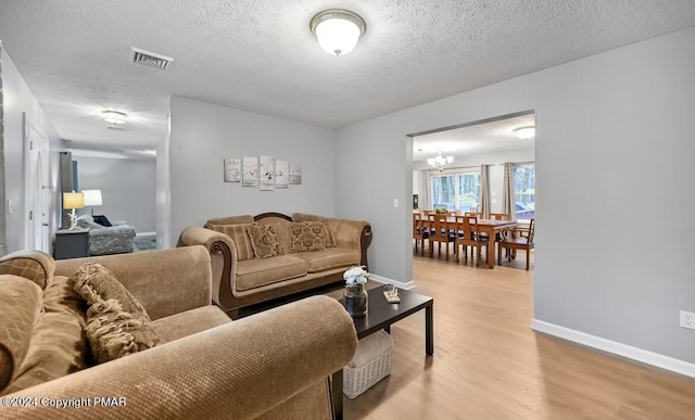 living area with baseboards, a textured ceiling, visible vents, and wood finished floors