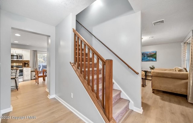 stairway with visible vents, a textured ceiling, baseboards, and wood finished floors