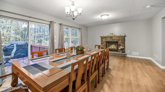 dining room with baseboards, visible vents, light wood-type flooring, a fireplace, and a notable chandelier