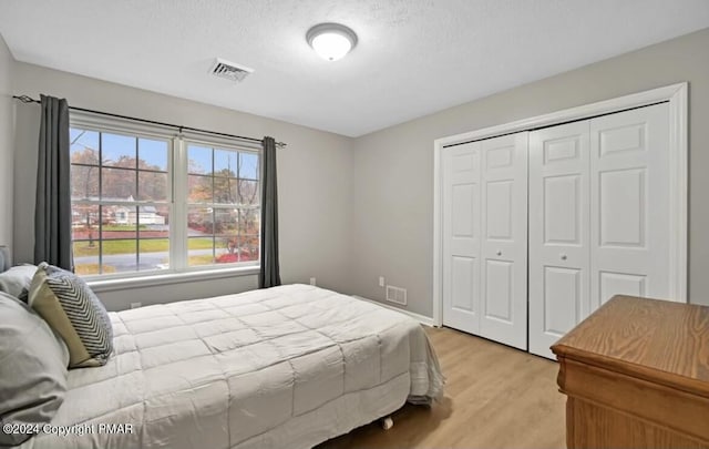 bedroom featuring a textured ceiling, a closet, light wood-type flooring, and visible vents