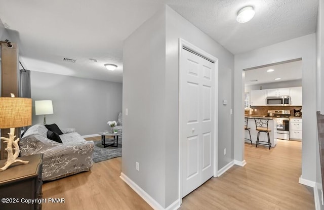 hallway with visible vents, light wood-style flooring, baseboards, and a textured ceiling