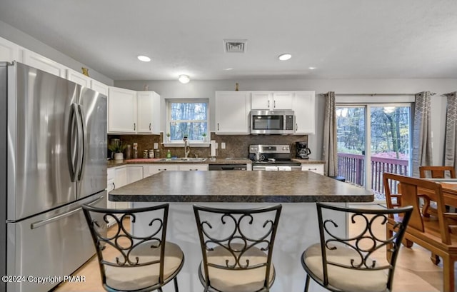 kitchen with stainless steel appliances, dark countertops, a sink, and a kitchen breakfast bar