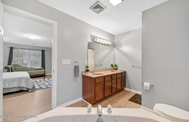 ensuite bathroom with visible vents, a tub with jets, wood finished floors, ensuite bathroom, and a sink