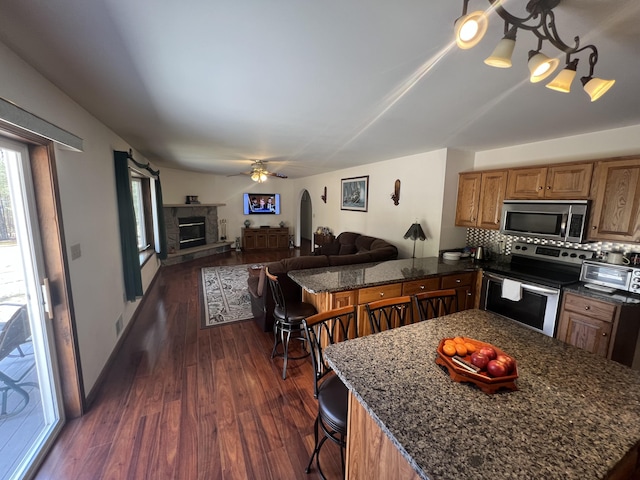 kitchen with a kitchen breakfast bar, dark wood-style floors, open floor plan, appliances with stainless steel finishes, and decorative backsplash