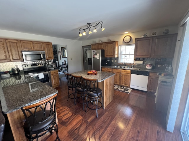 kitchen featuring brown cabinets, a breakfast bar, a sink, stainless steel appliances, and dark wood-style flooring