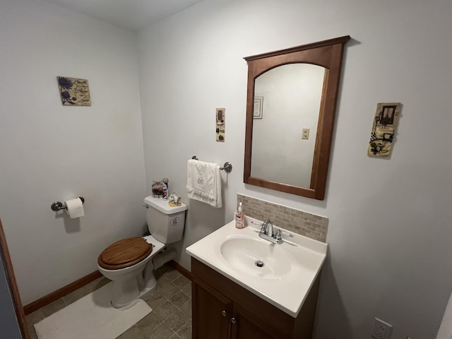 half bathroom with vanity, decorative backsplash, toilet, and baseboards